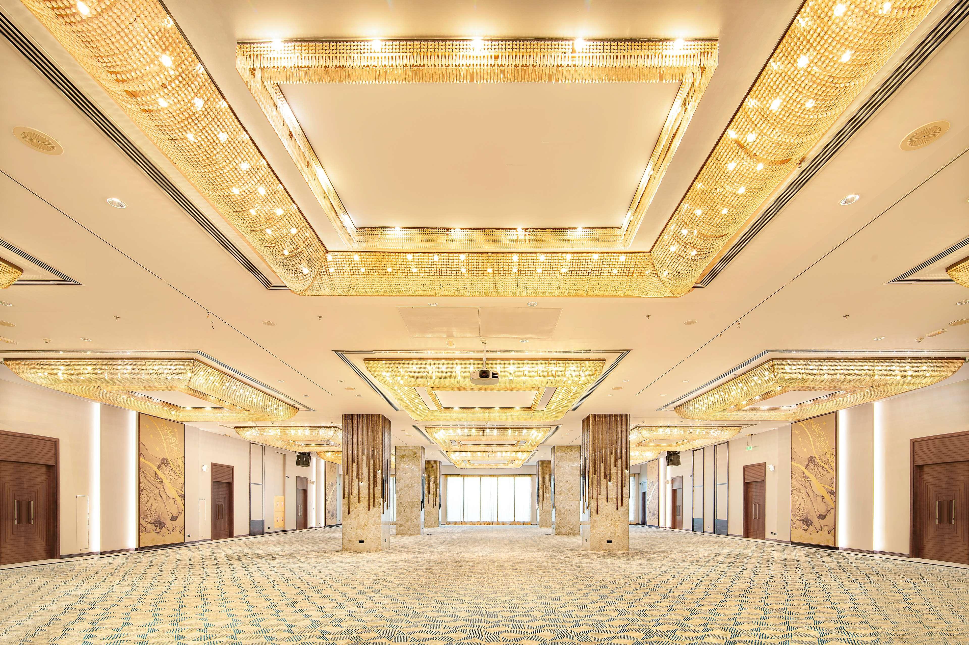 Radisson Blu Hotel & Resort, Abu Dhabi Corniche Exteriör bild The photo shows a spacious, elegantly designed interior, likely a banquet or conference hall. The ceiling features a luxurious design with intricate lighting elements that give off a warm glow. The floor is covered with a patterned carpet in soft col